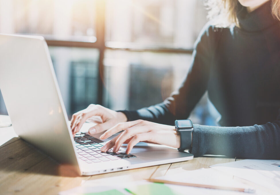 Work Process in Modern Office. Young Account Manager Working at Wood Table with New Business Project.Typing Contemporary Laptop keyboard,Wearing Smartwatch. Horizontal. Film effect.Blurred background.